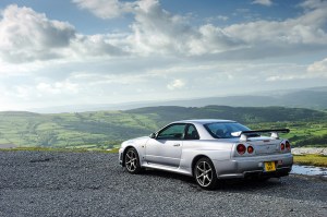 A Nissan Skyline GT-R R34 looking out over a mountainous landscape.